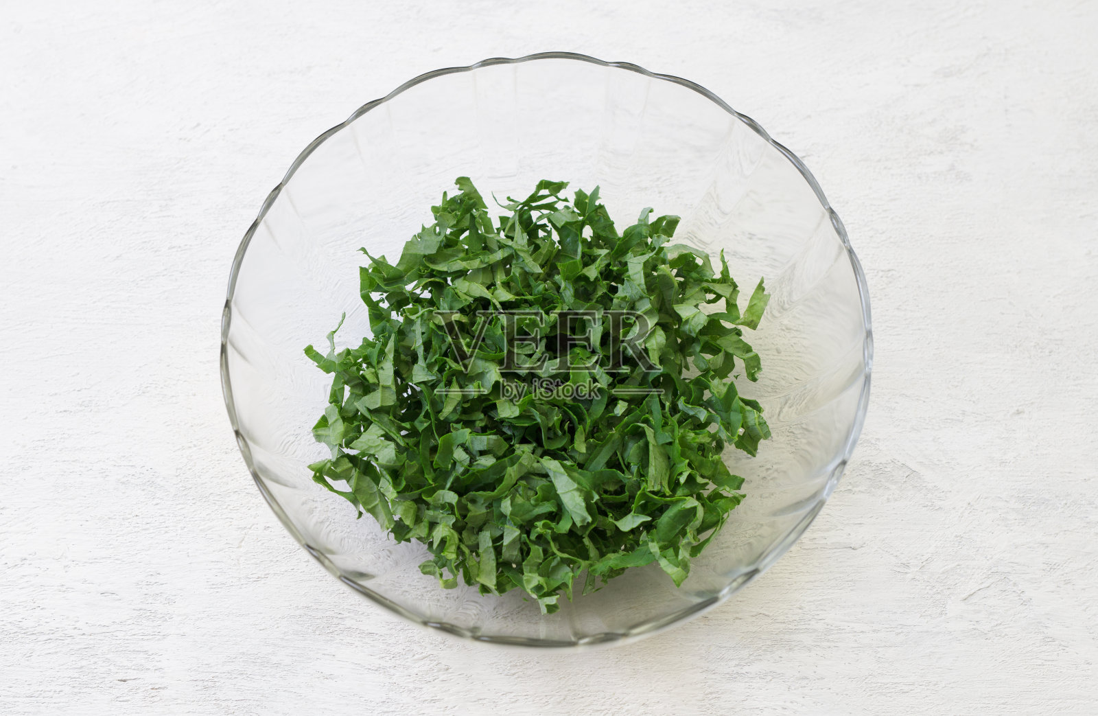 切碎的甘蓝叶，加盐压碎，放在透明的碗里，背景是浅灰色的。健康排毒食物照片摄影图片