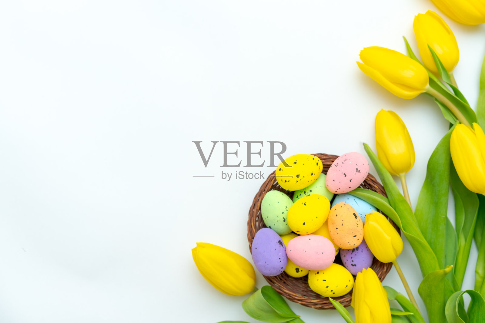 柳条篮子里装着五颜六色的复活节彩蛋，白色背景上是黄色的郁金香。照片摄影图片