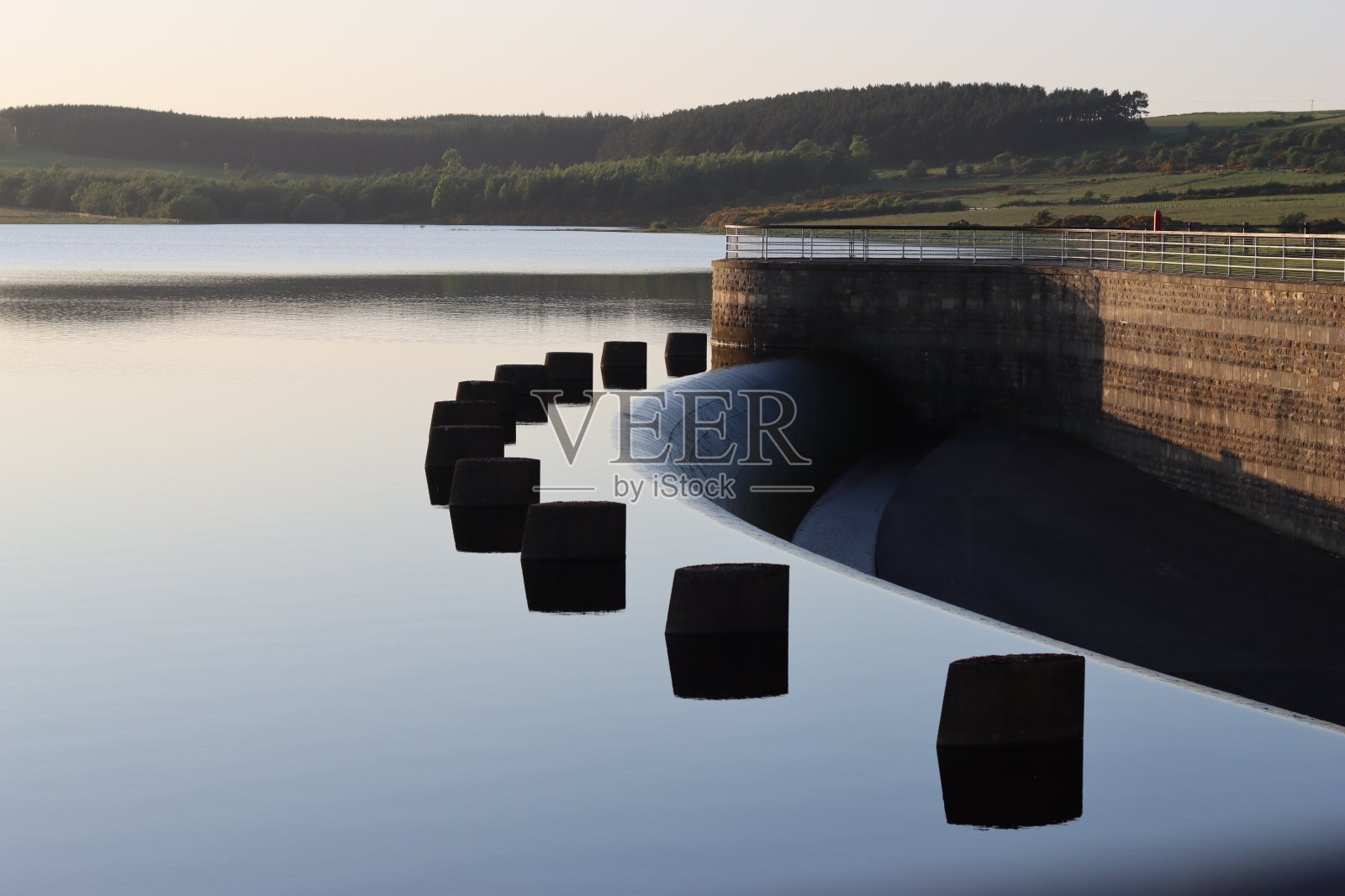 日落时水库溢洪道对面的景色，在静止的水中有完美的倒影照片摄影图片