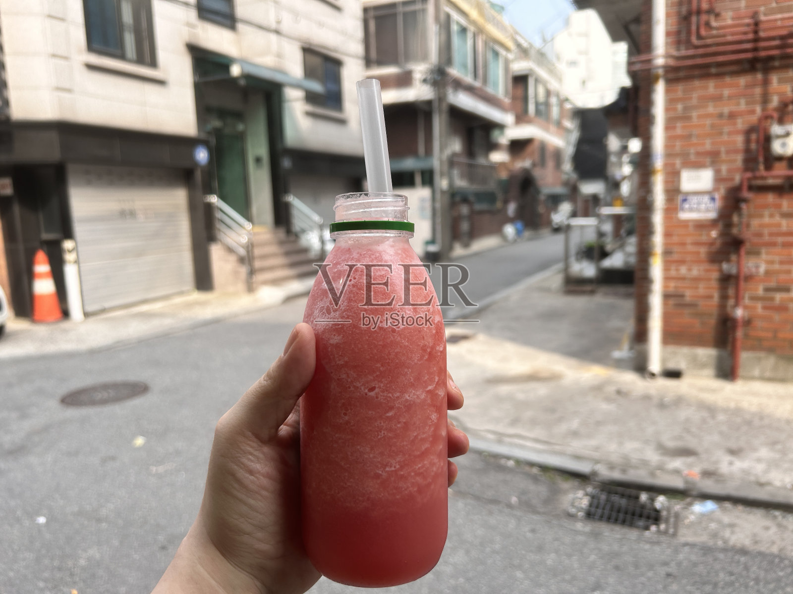 女人手里拿着一瓶红色的冰沙，西瓜汁照片摄影图片