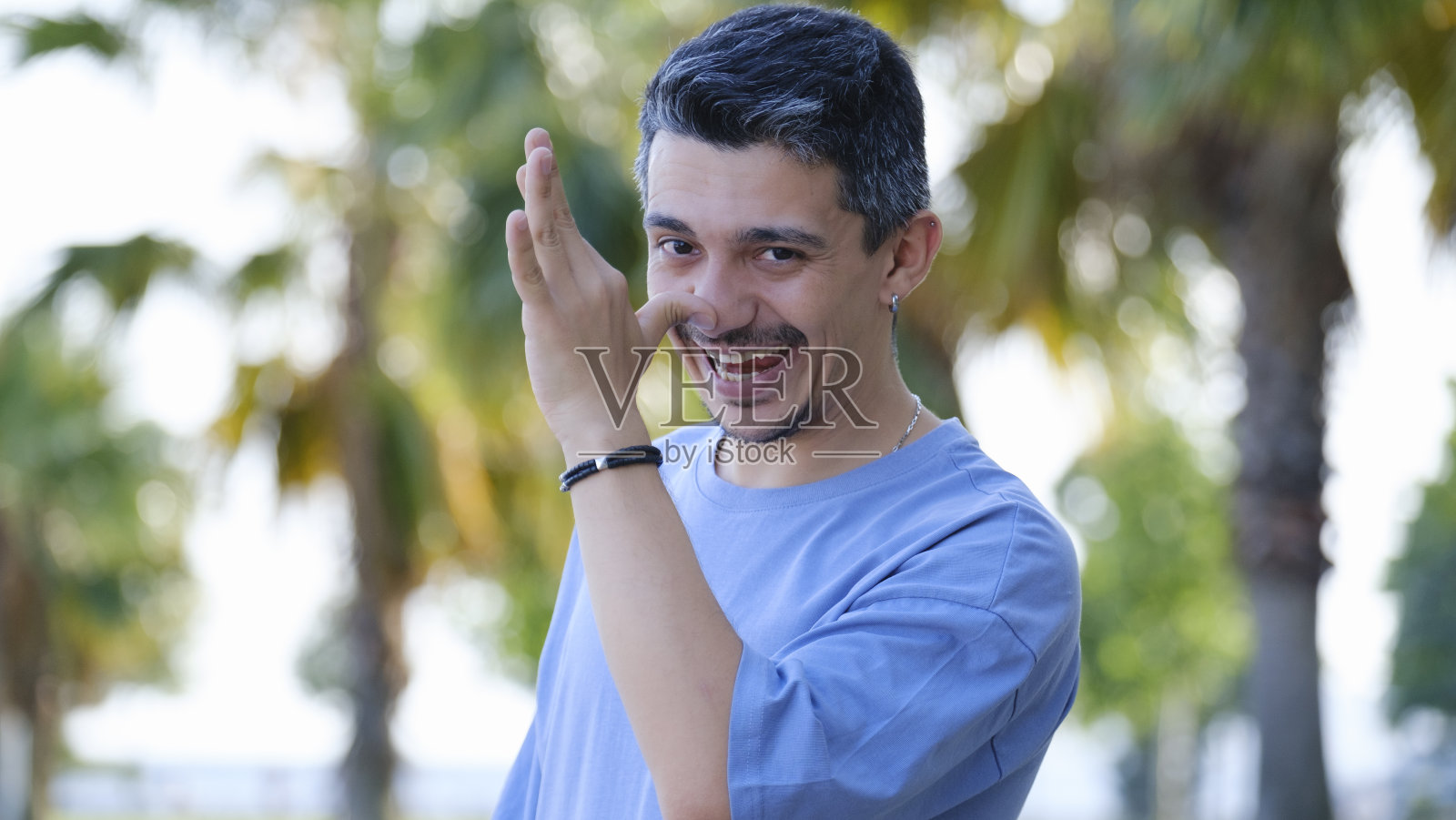 一个黑头发的男人站在树林里，对着镜头做着孩子气的鬼脸照片摄影图片