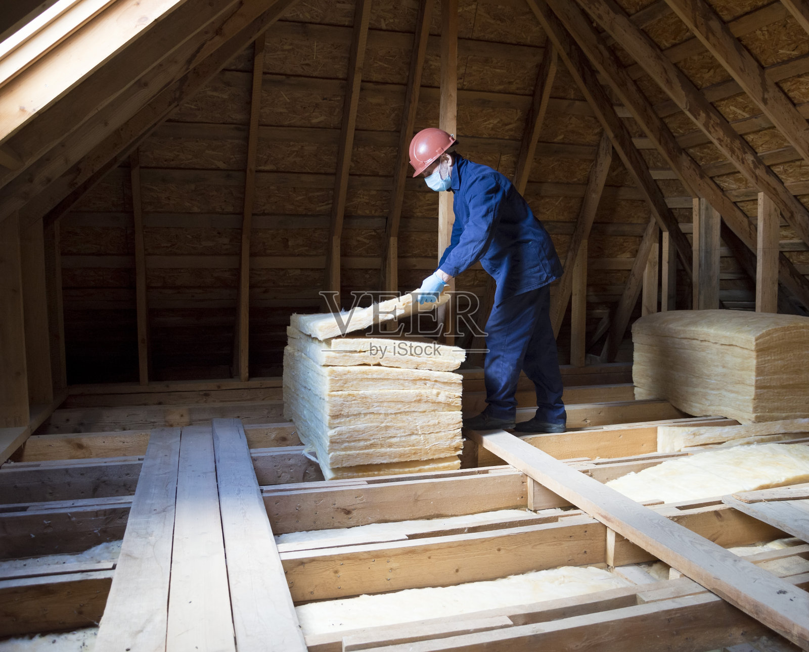 屋顶保温。一名工人把玻璃棉绝缘材料放在阁楼上。照片摄影图片