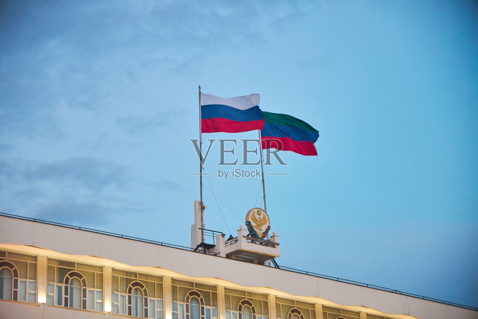 达吉斯坦共和国和俄罗斯国旗在城市中心广场的共和国行政大楼上。照片摄影图片