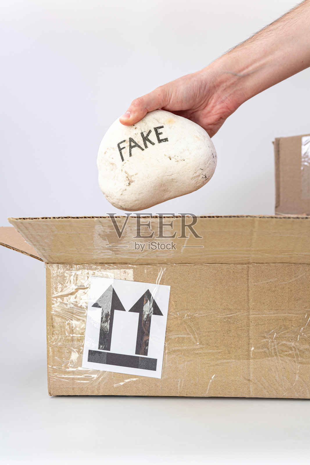 手将带有FAKE线的石头放入纸板箱中。照片摄影图片