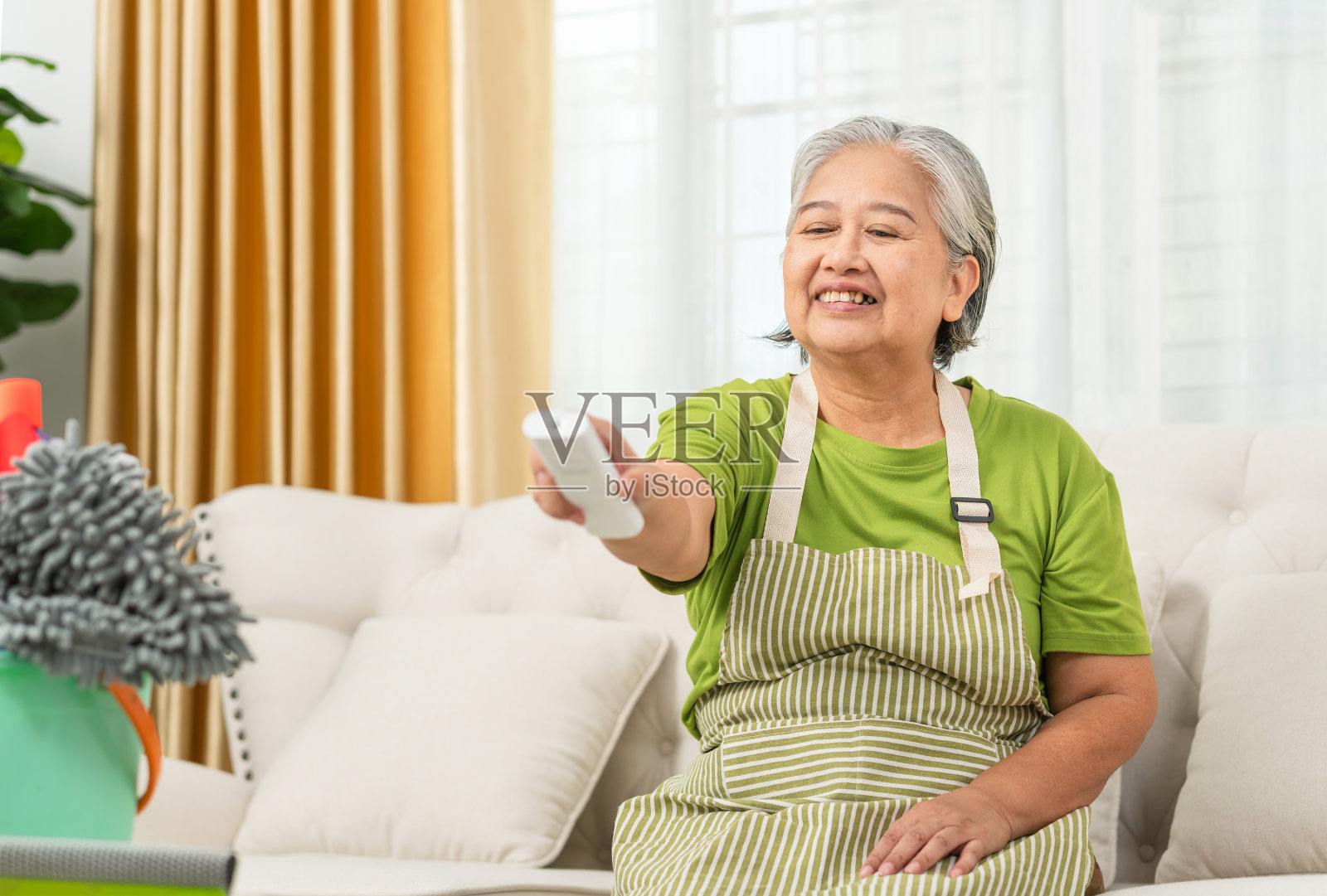 微笑的亚洲老妇人在客厅拿着空调遥控器，女人打开空调照片摄影图片