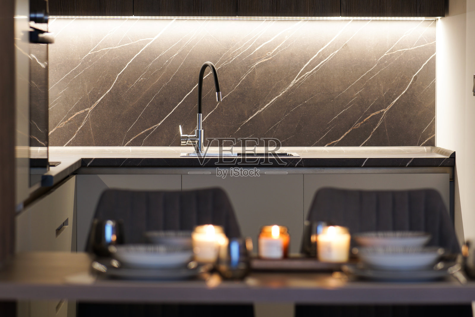 背景是现代干净的厨房，前景是模糊的餐桌，夜间照片是开着灯的照片摄影图片