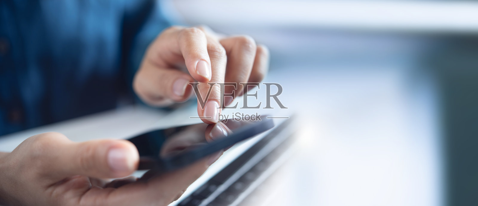 特写，女士在办公桌上使用手机和笔记本电脑。商务女性上网，使用智能手机，在办公室用笔记本电脑工作照片摄影图片