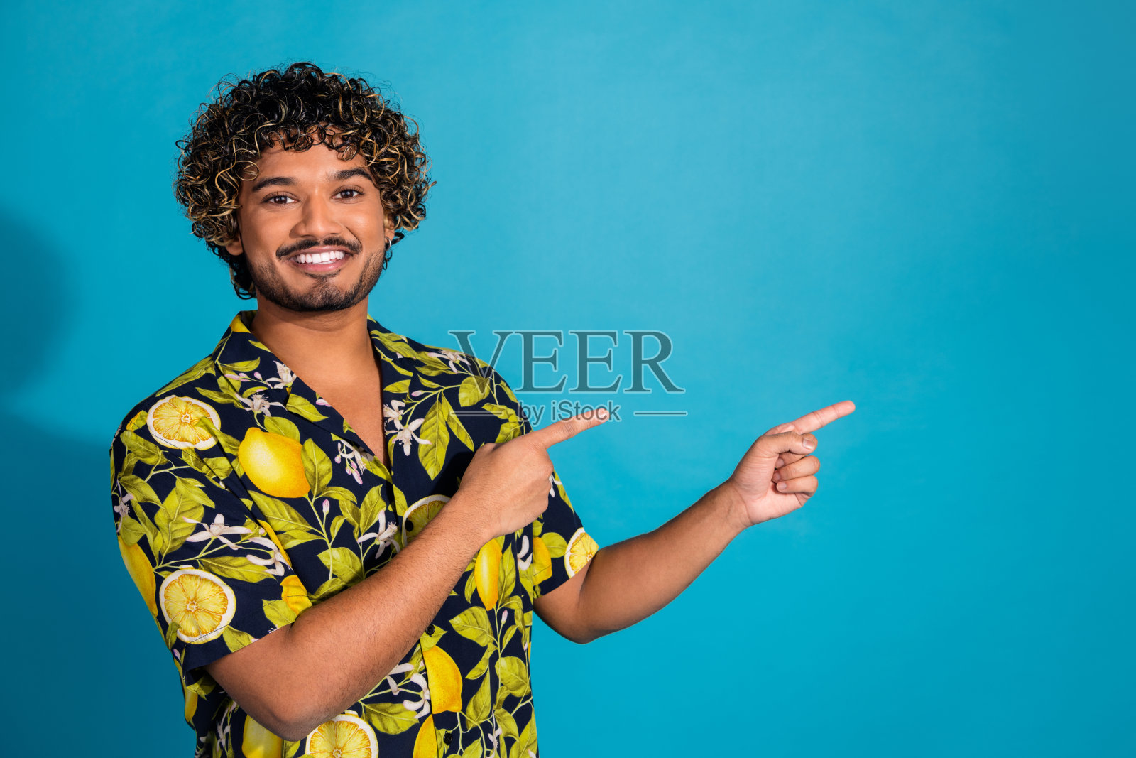 照片的好心情男子与胡子波浪发型穿着印花衬衫表明在出售空空间孤立的蓝色背景照片摄影图片