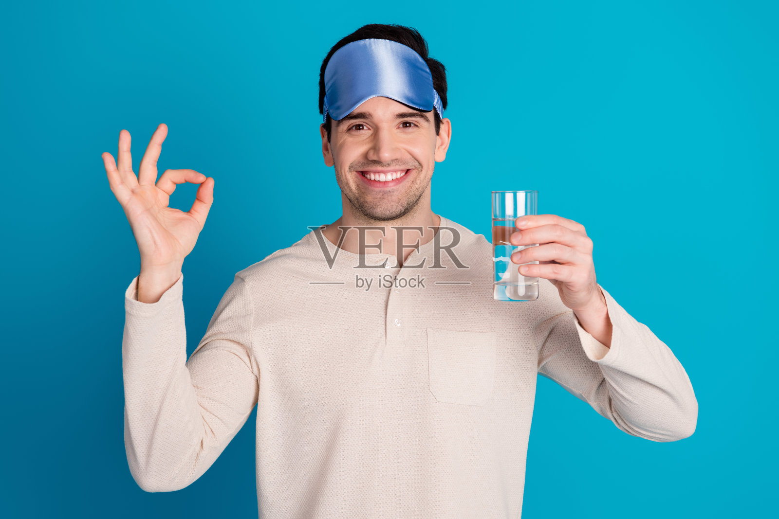 漂亮的年轻人的肖像拿着水显示好穿睡衣孤立的蓝色背景照片摄影图片