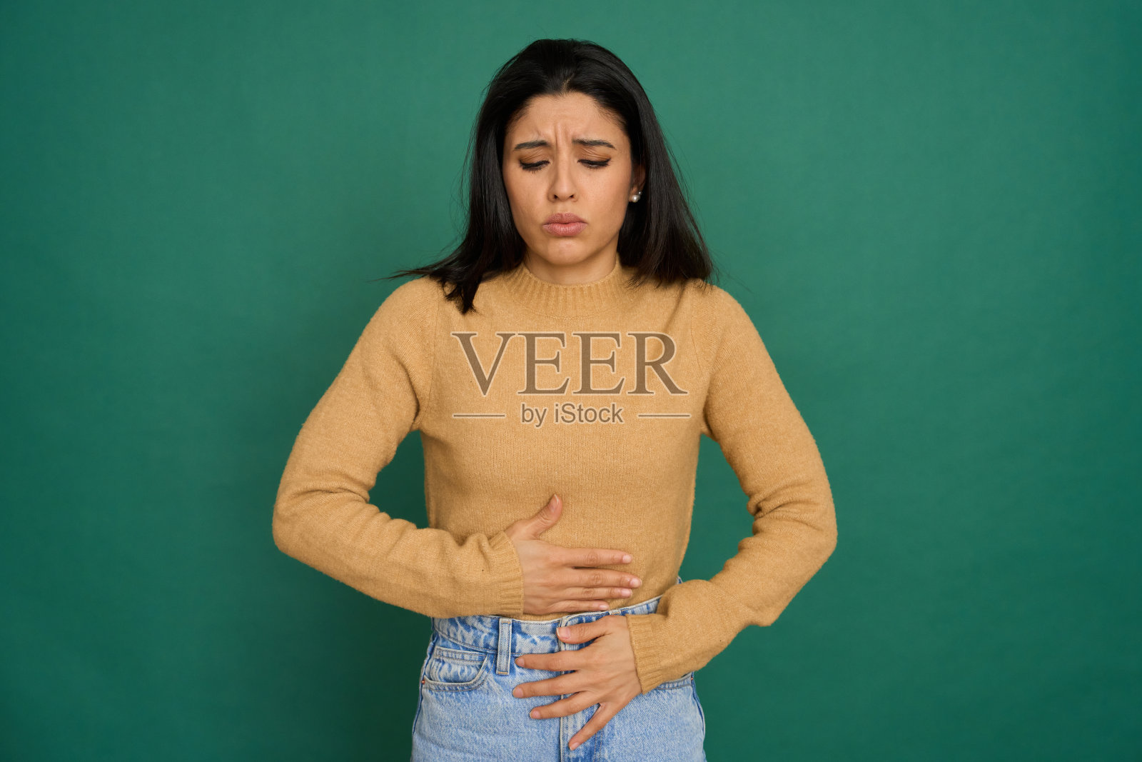 在绿色背景上，一个年轻的女人正在忍受着强烈的胃痛照片摄影图片