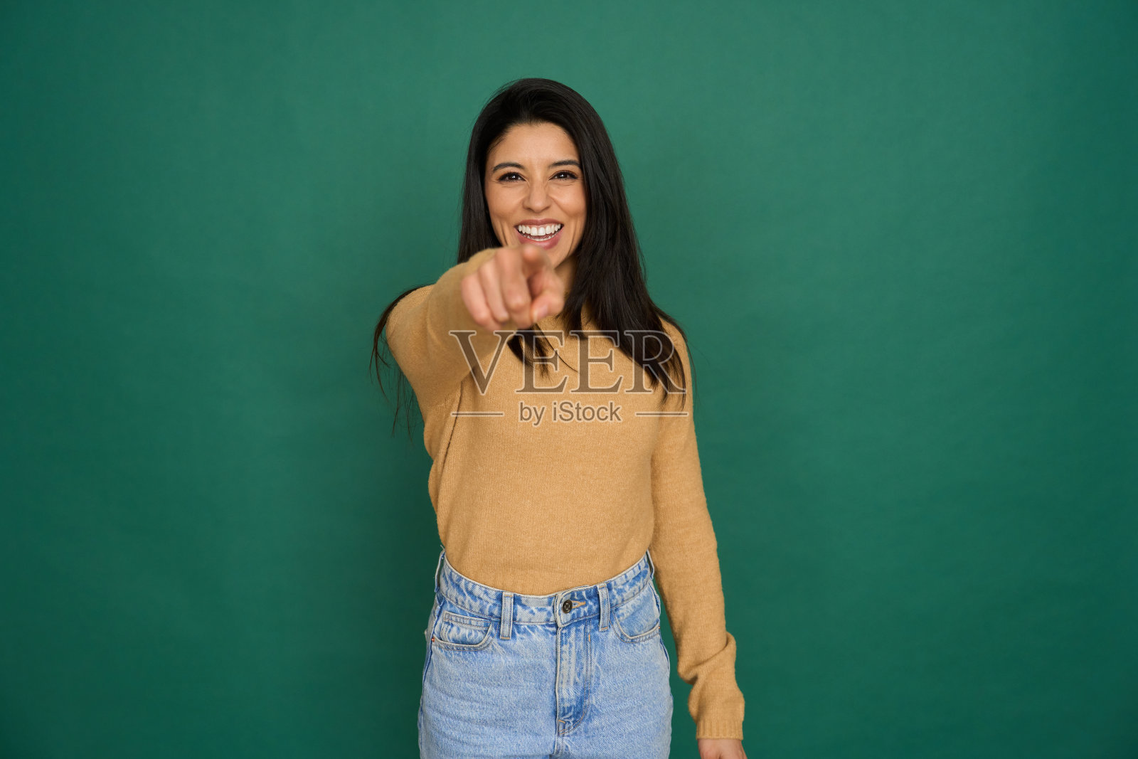 年轻的成年女子指着你，在绿色背景上微笑照片摄影图片