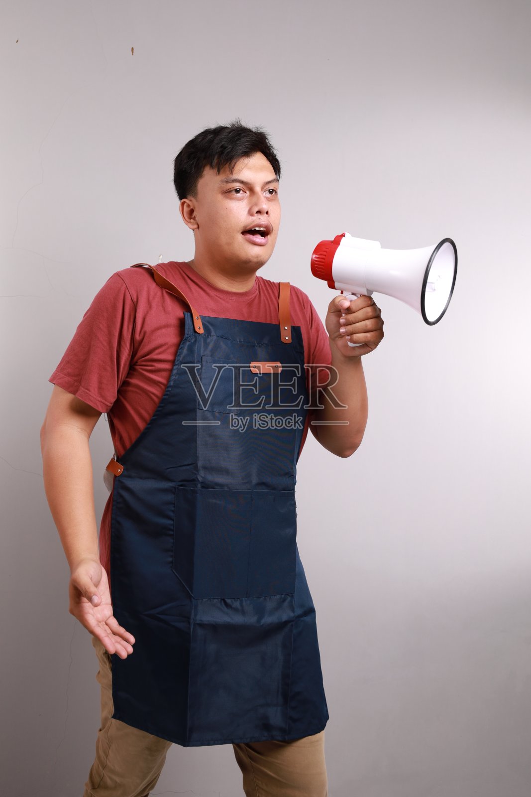 年轻的亚洲男子，咖啡师，酒吧服务员，穿着蓝色围裙，站在咖啡店工作，手里拿着扩音器照片摄影图片