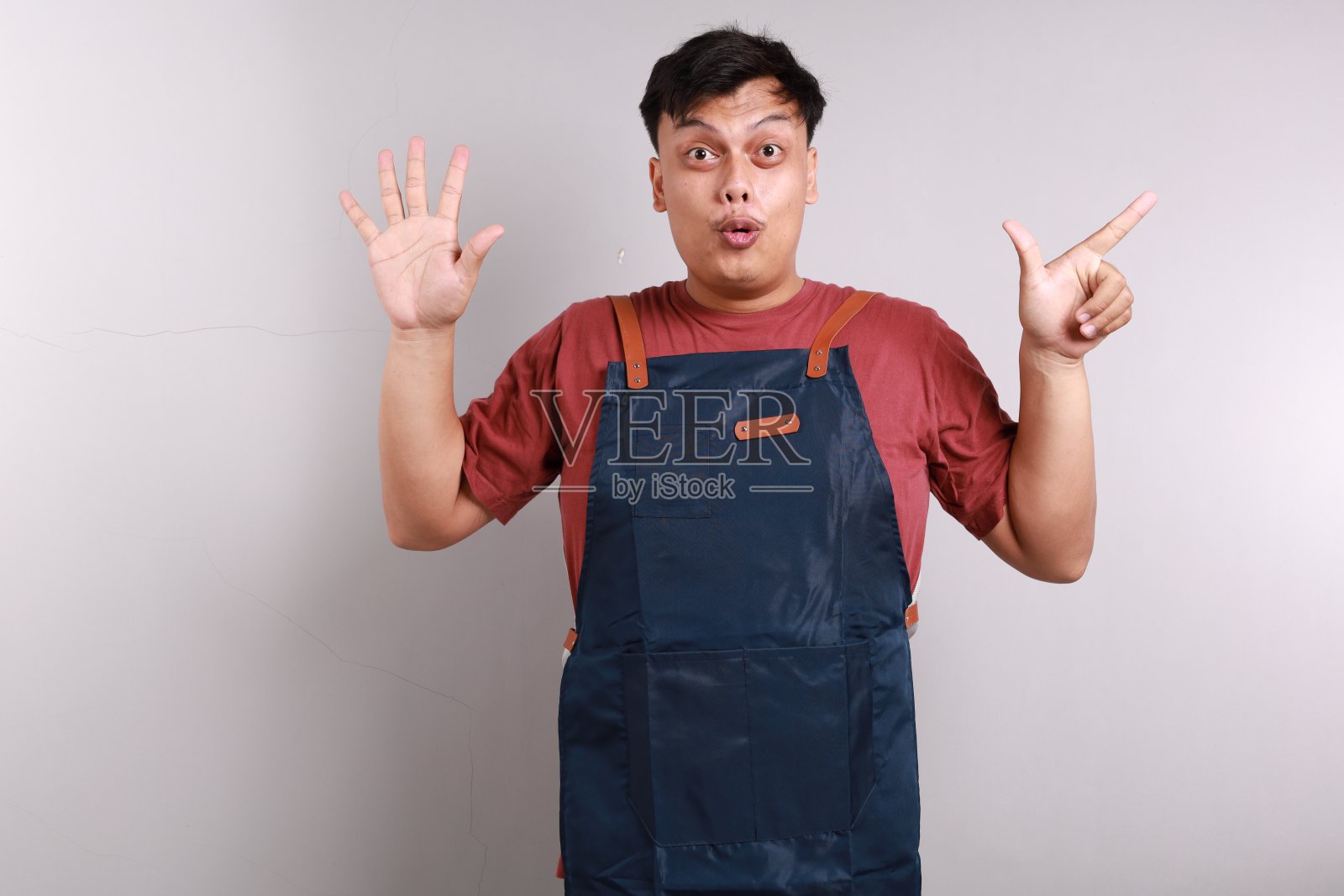 身穿白底围裙的亚洲青年露出7根手指，脸上露出兴奋和快乐的表情照片摄影图片