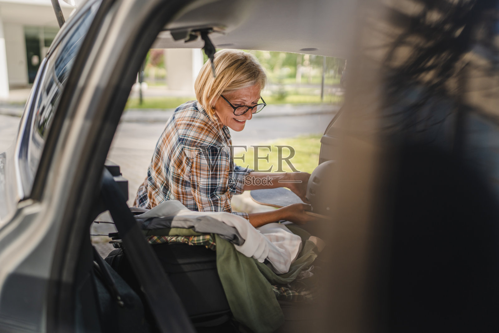 成熟的金发女子旅行时从汽车后座拿东西照片摄影图片