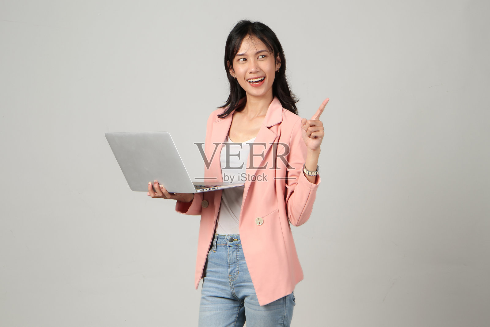 快乐的亚洲女人穿着正式的休闲装，拿着笔记本电脑，用手指指着孤立的背景照片摄影图片