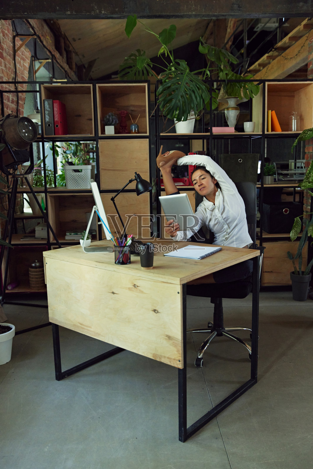 我们,的人。上班族以伸展的姿势坐在办公桌前，在现代办公环境下用平板电脑工作照片摄影图片