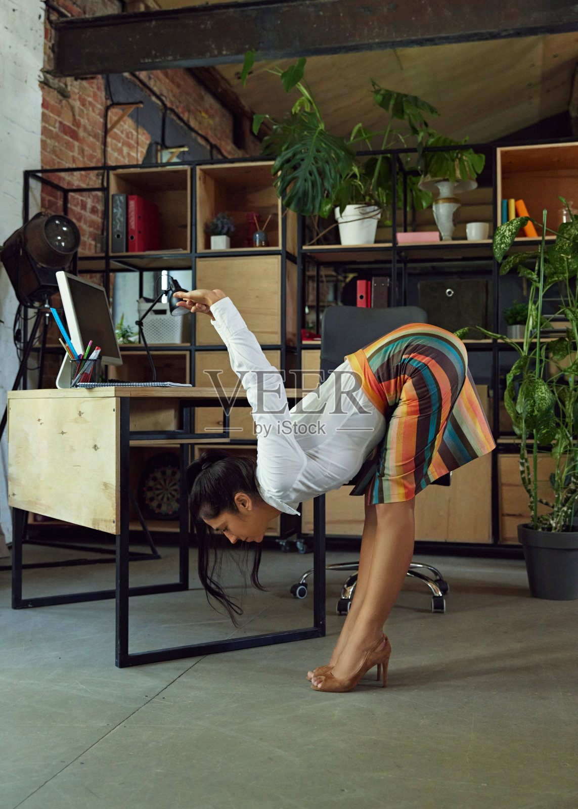 女性，办公室职员，穿着正装，一边工作一边在办公桌前做伸展运动。现代办公环境。安慰照片摄影图片