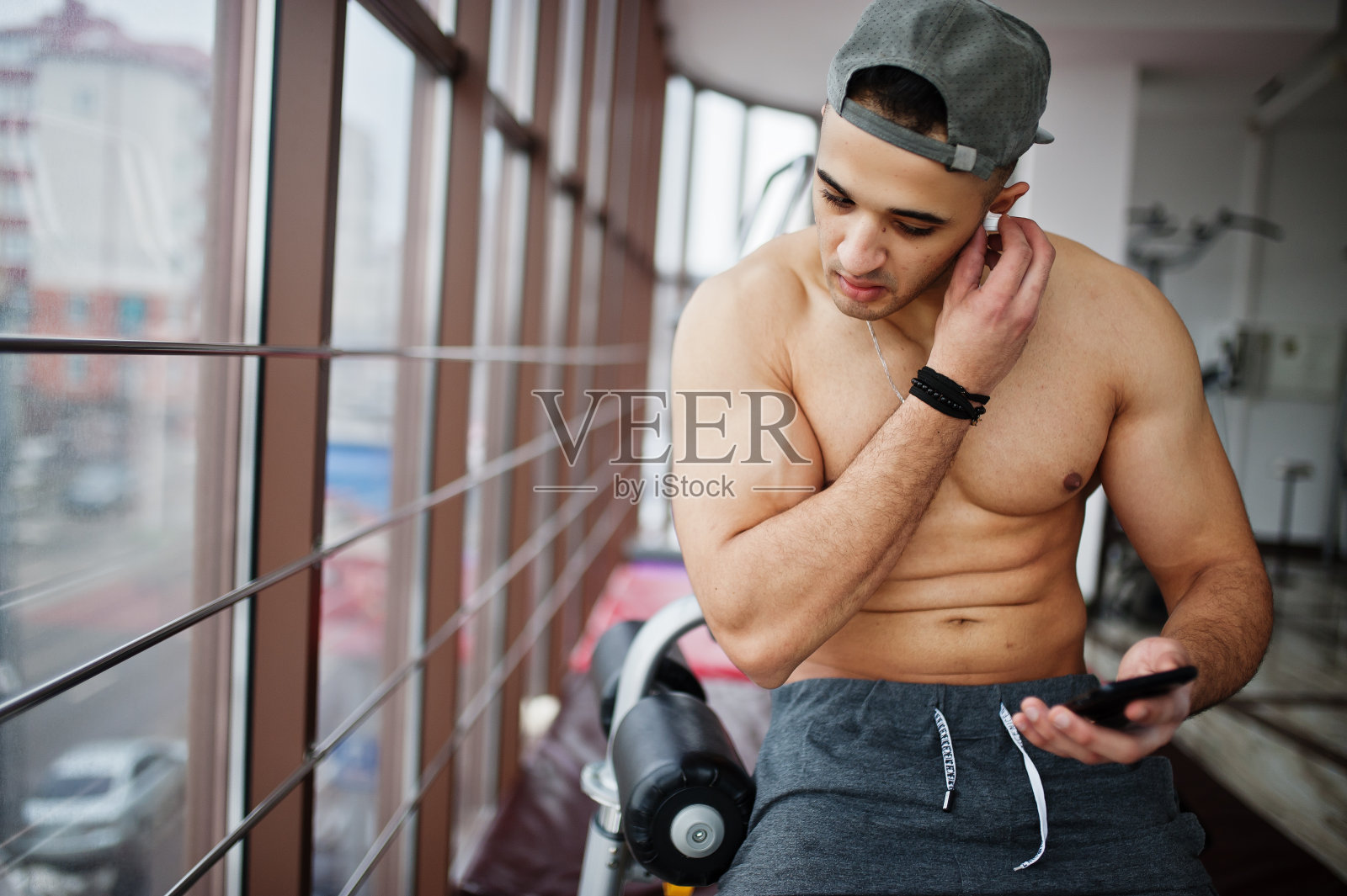 健美和肌肉发达的阿拉伯男子在健身房摆姿势，拿着手机。照片摄影图片