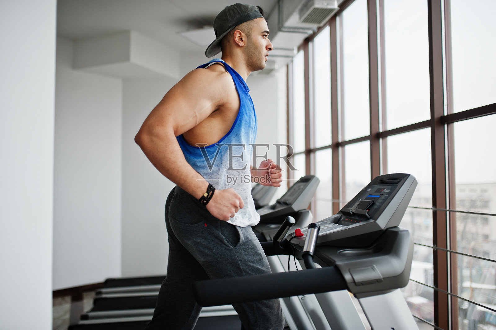 健美、肌肉发达的阿拉伯男子在健身房的跑步机上跑步。照片摄影图片
