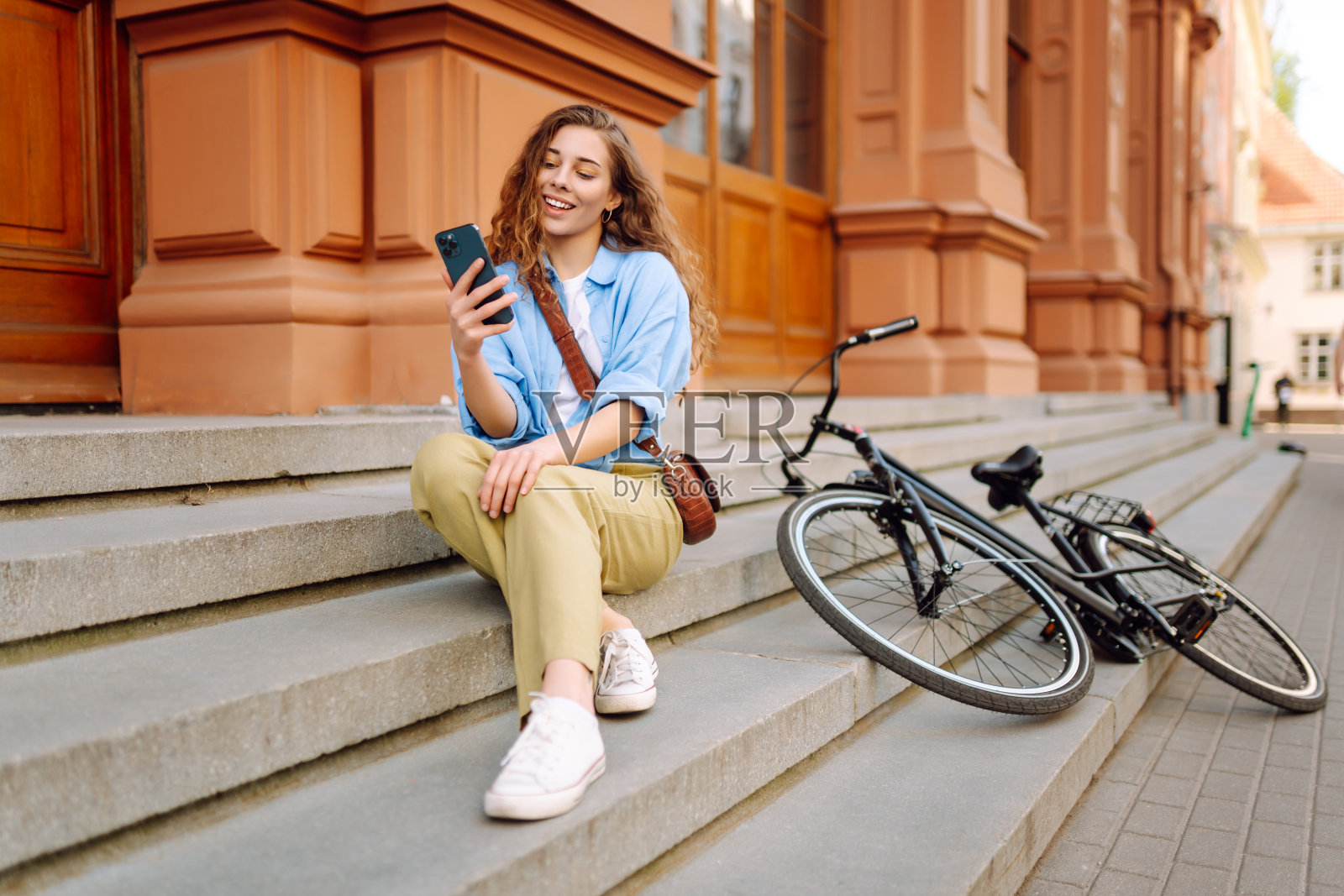 年轻女子边骑自行车边玩手机。照片摄影图片