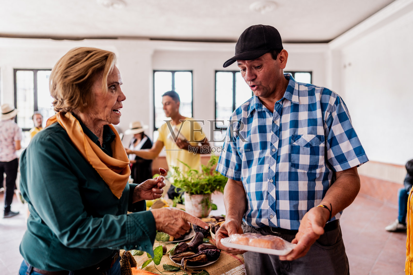 一位资深女游客在哥伦比亚当地产品商店与一位购买辣味香肠的推销员交谈照片摄影图片