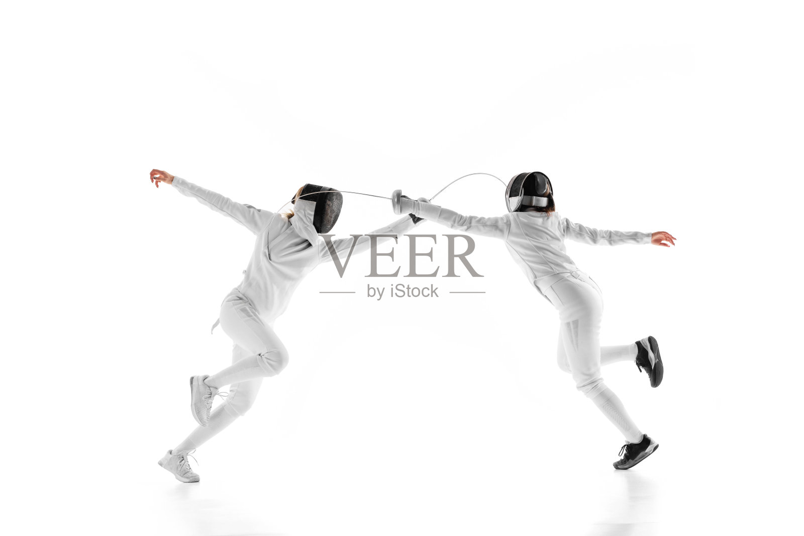 在准备比赛的过程中，两名女击剑运动员正面交锋，每个人都试图在白色的工作室背景下胜过对方。运动。照片摄影图片