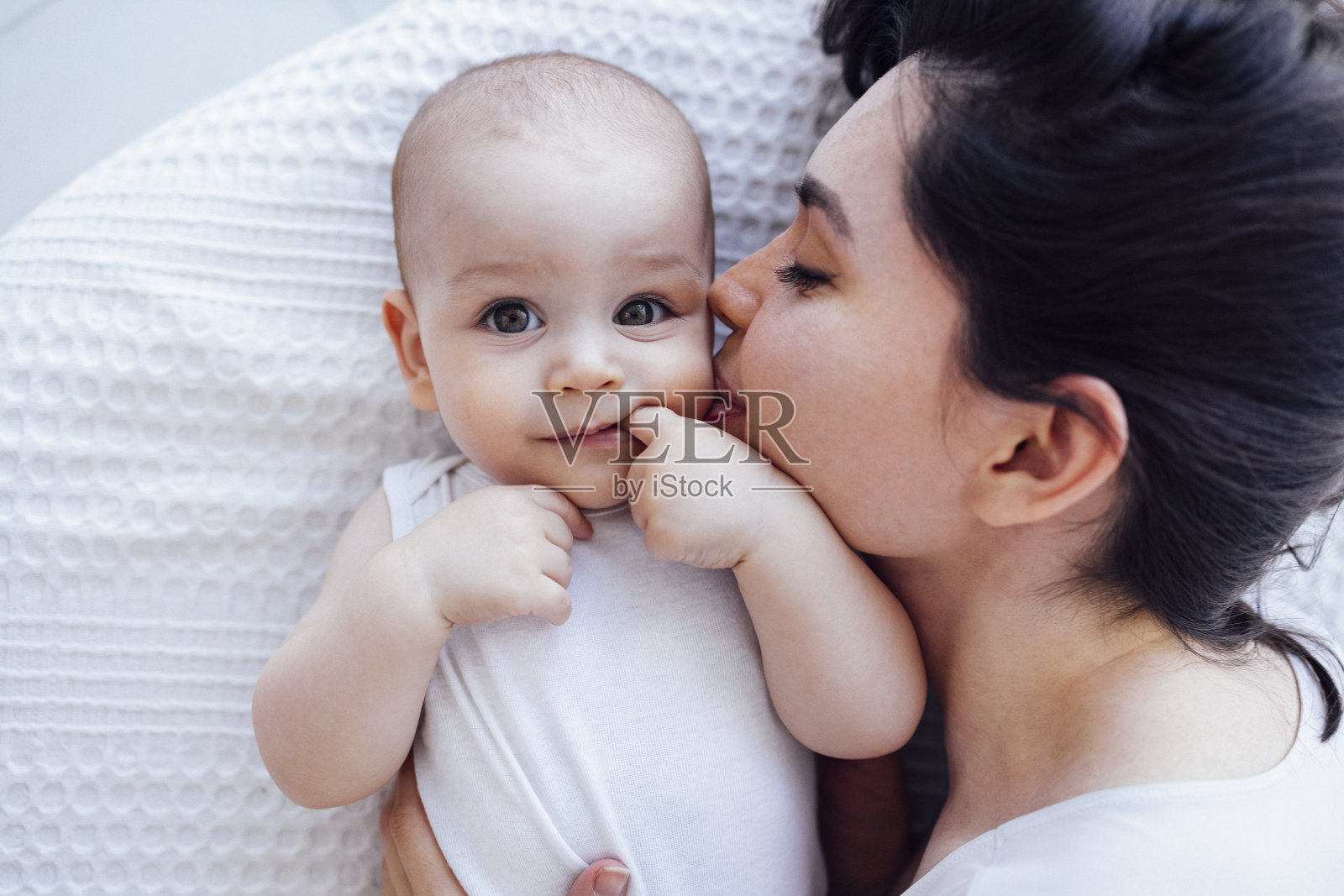 年轻美丽的母亲亲吻她可爱的孩子的脸颊。一个黑发白人女人用脸抚摸着她微笑的孩子。照片摄影图片