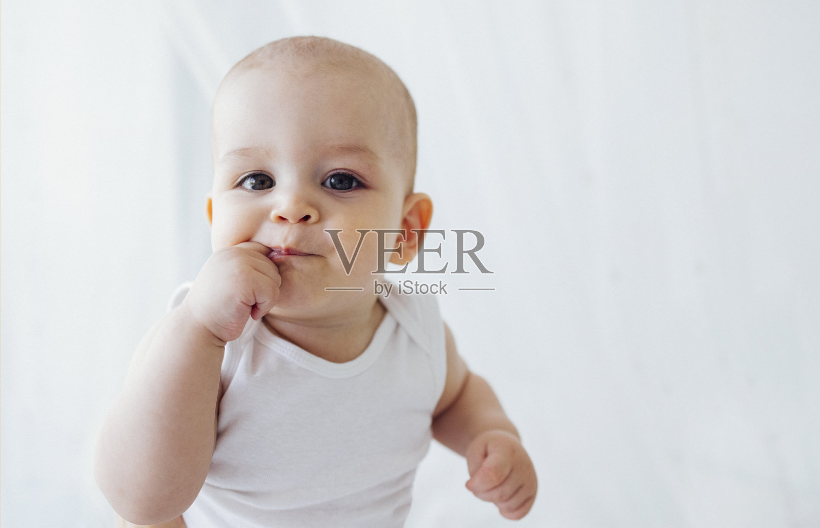 可爱宝宝的肖像特写。可爱的小孩舔着手指看着镜头。照片摄影图片