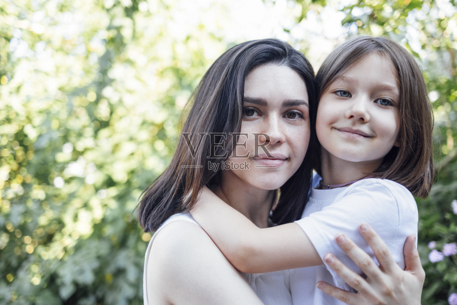 年轻迷人的女子抱着她可爱的小女儿在户外的花园里绿树成荫。照片摄影图片