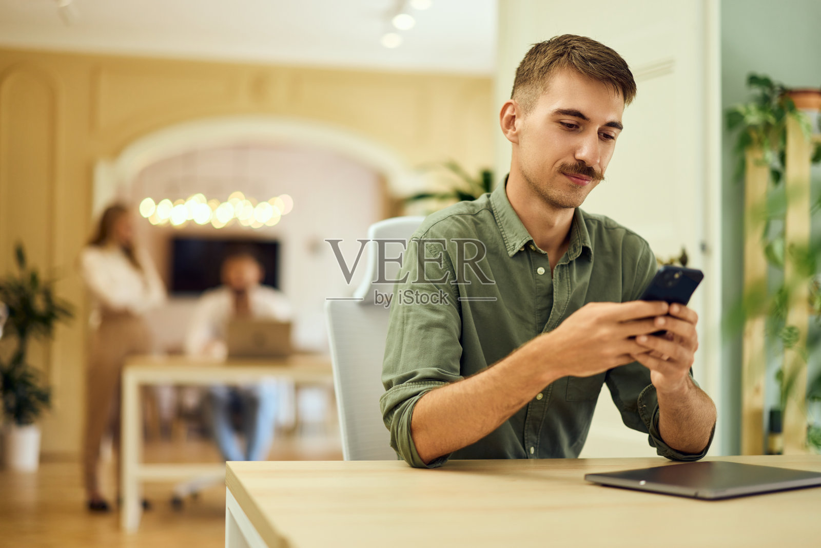 一名留胡子的男子在联合办公空间工作时使用手机。照片摄影图片