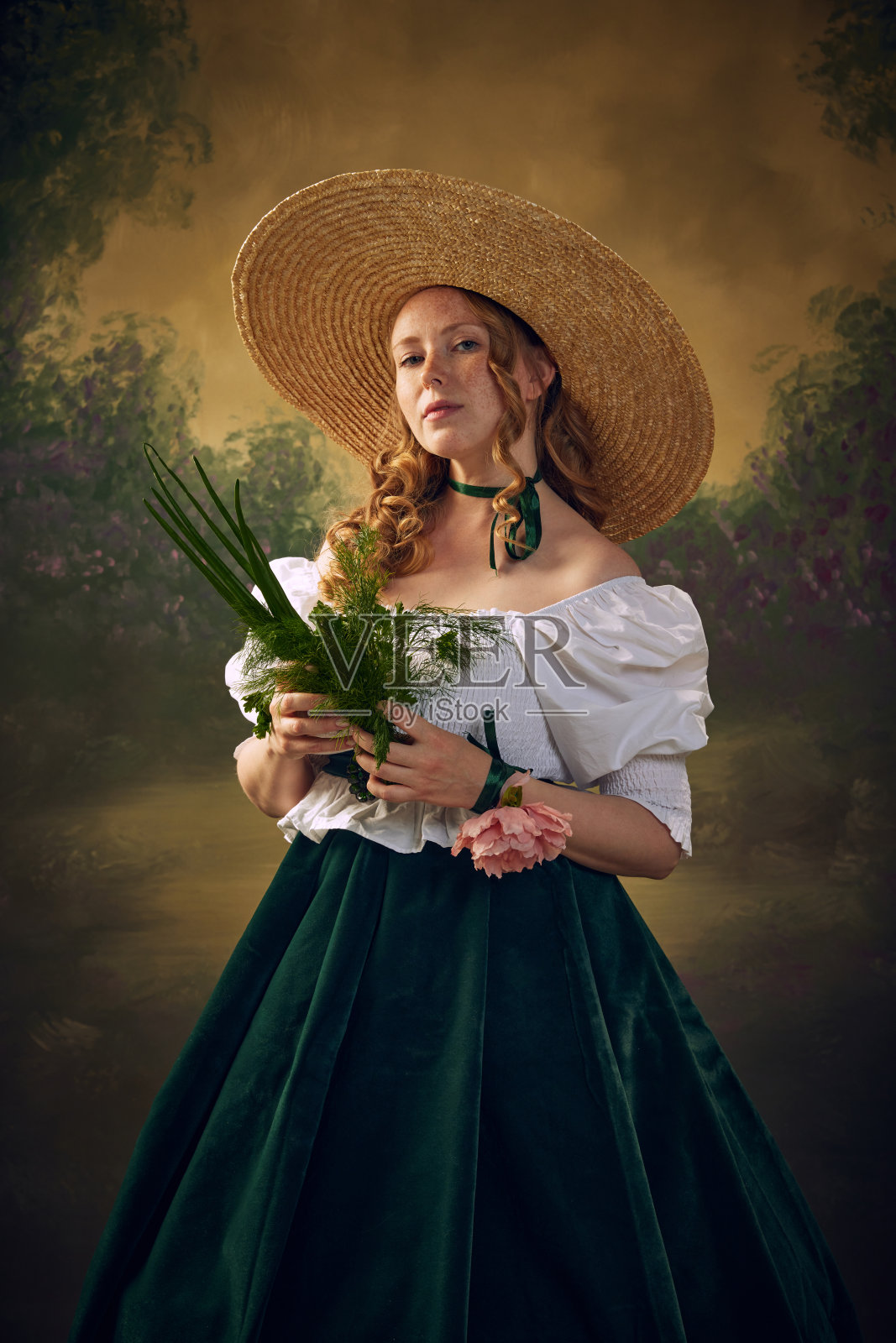 美丽的年轻女子的肖像，穿着文艺复兴风格的服装，戴着大帽子，站在绿色背景下的绿色花束上照片摄影图片