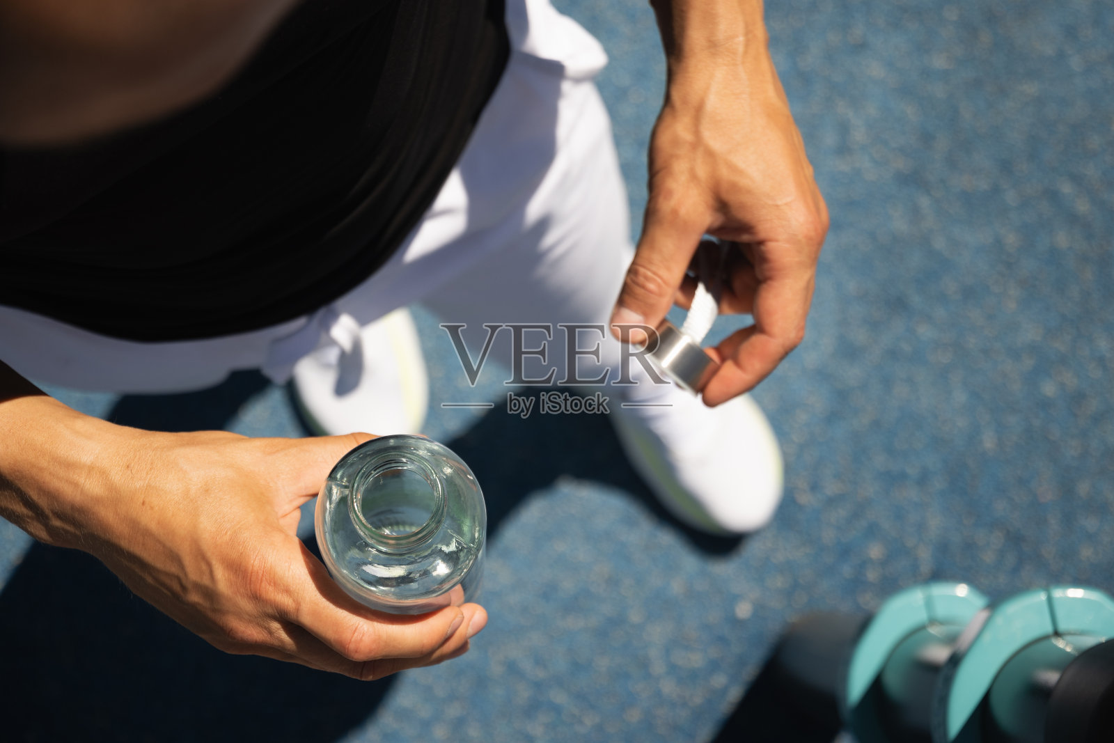 在运动场上，运动员手里拿着一瓶清凉的水。锻炼时的水分平衡。照片摄影图片