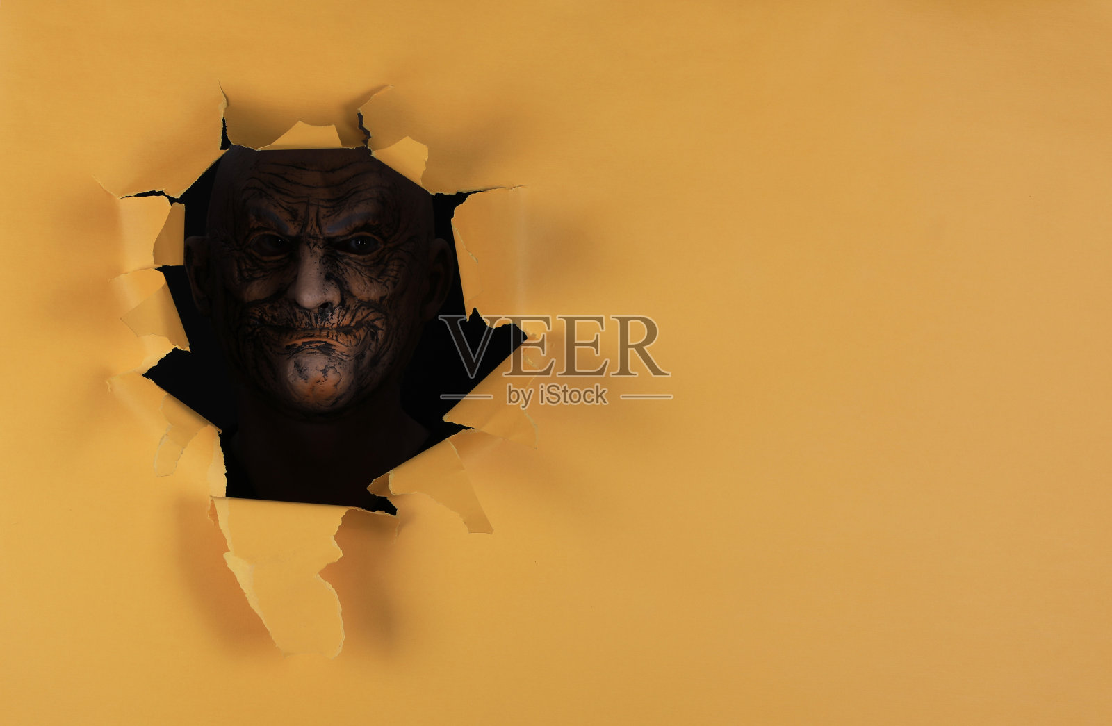 戴着怪物面具的人在黄色纸洞里照片摄影图片