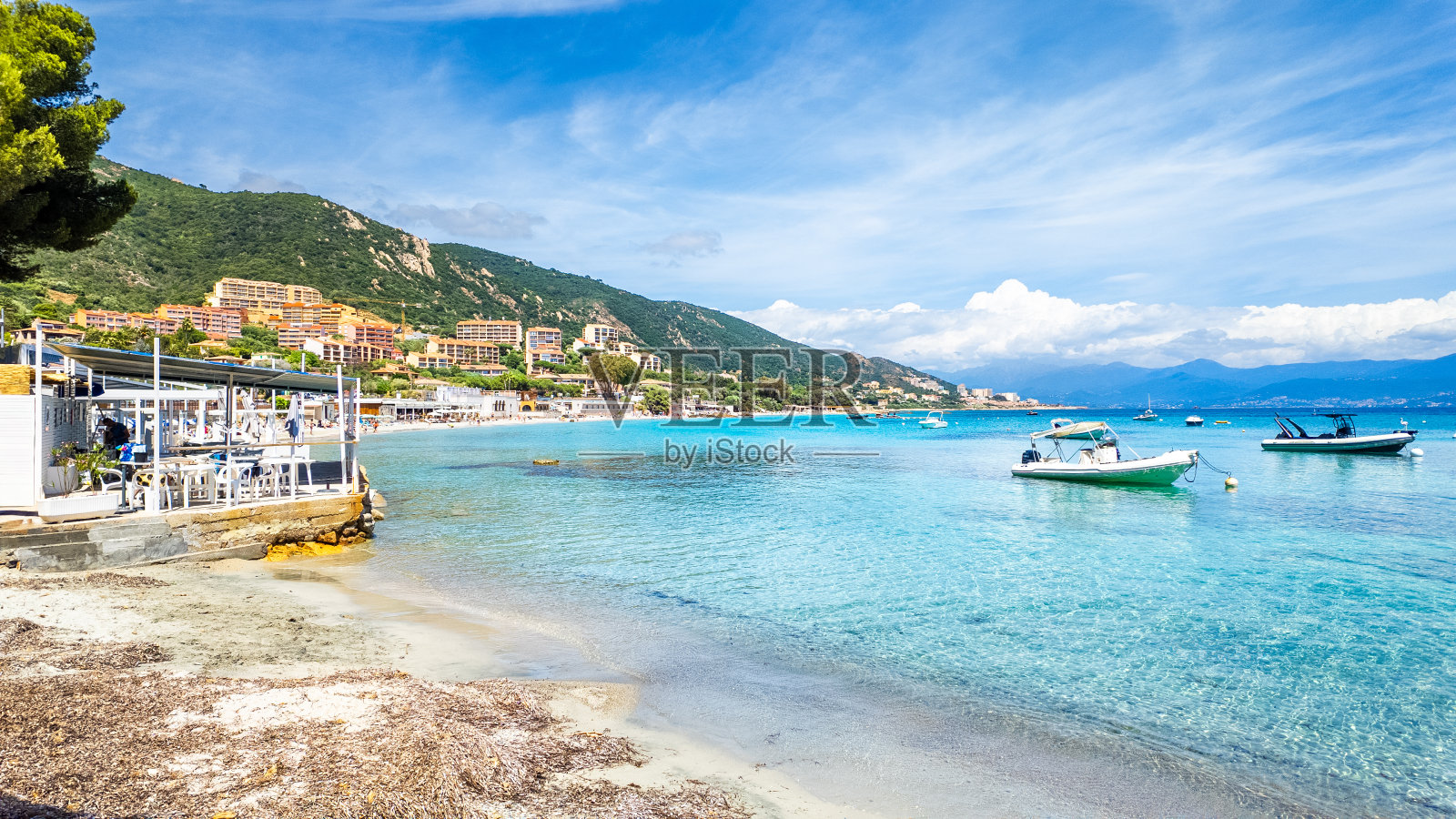 船停泊在马里内拉海滩与风景秀丽的海岸村和清澈的蓝色水域，科西嘉岛。照片摄影图片