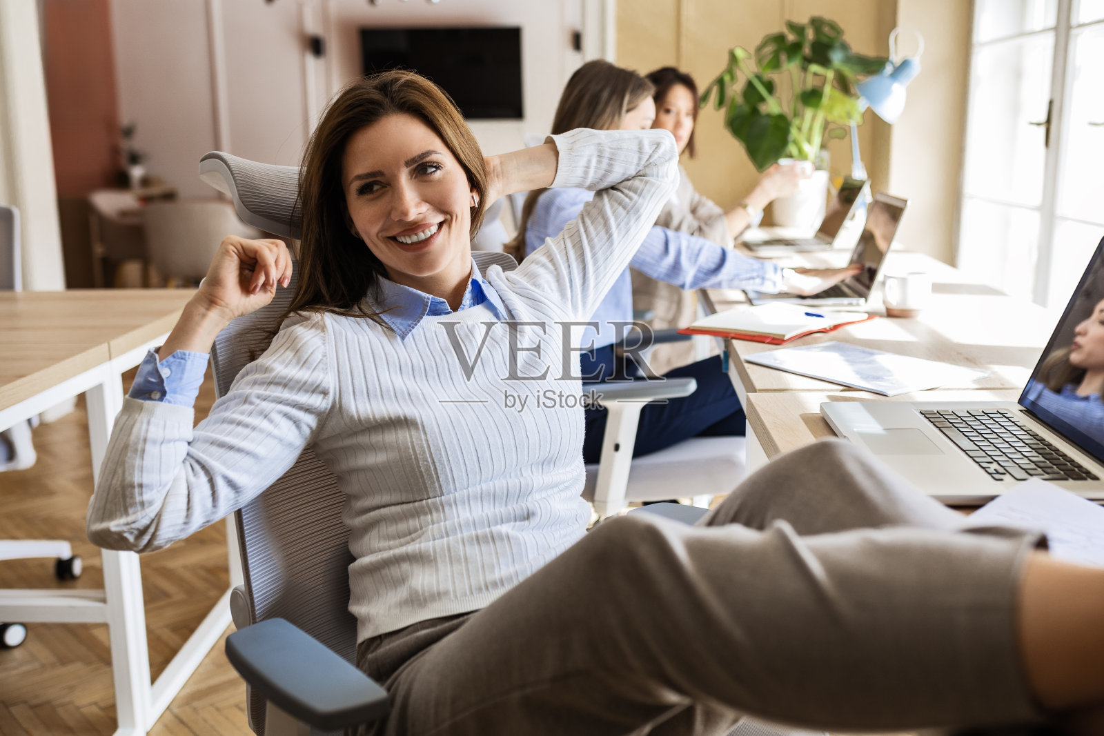 脚搁在桌子上看着镜头的女商人照片摄影图片