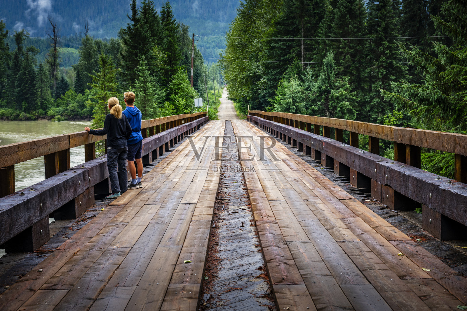 加拿大大不列颠哥伦比亚省森林中的木桥上的两个人照片摄影图片