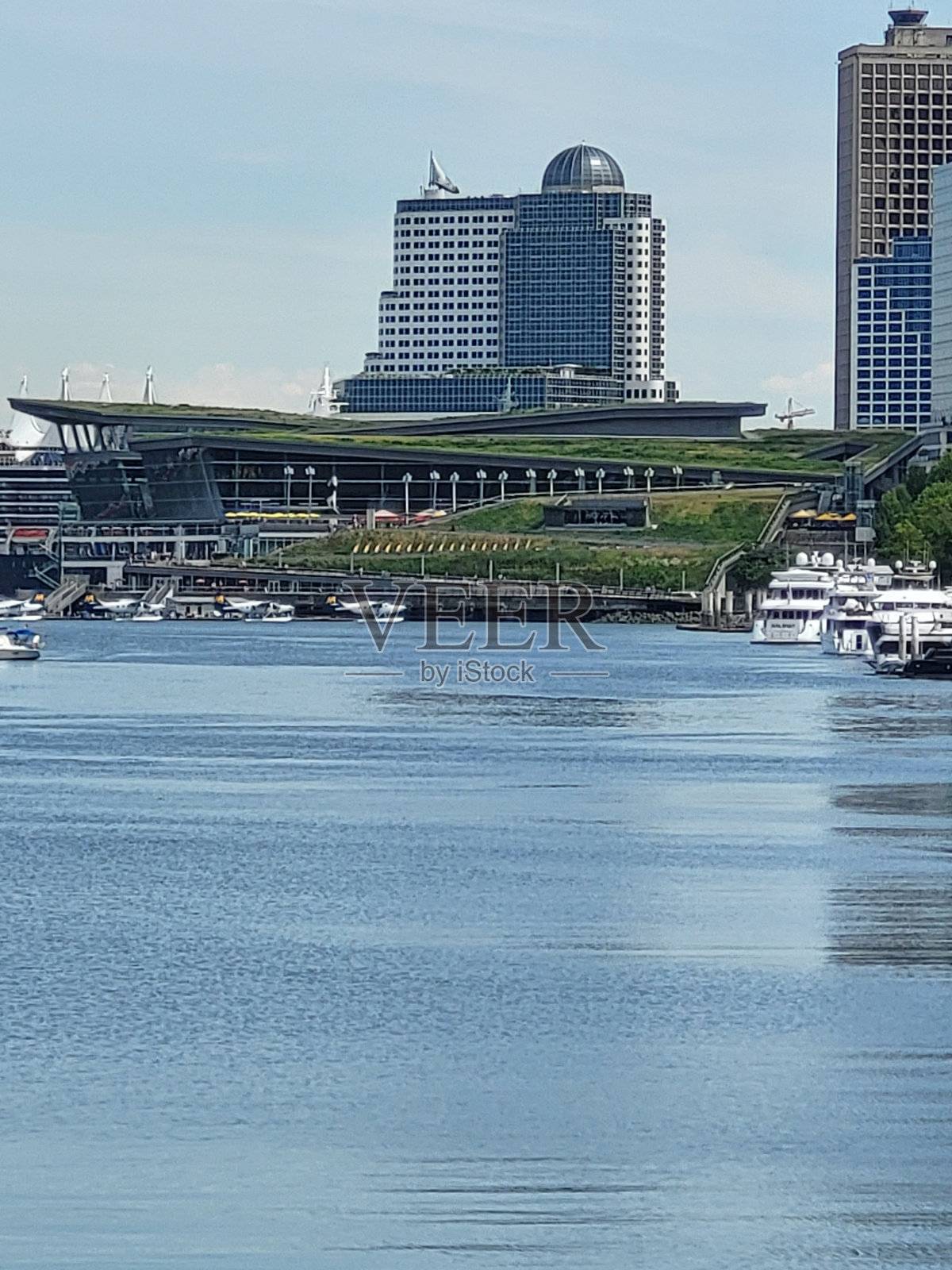 从温哥华斯坦利公园海堤绿道的有利位置，可以看到加拿大广场、会议中心和海港航空，有水上飞机和帆船在海港平静的蓝色海水中航行。照片摄影图片