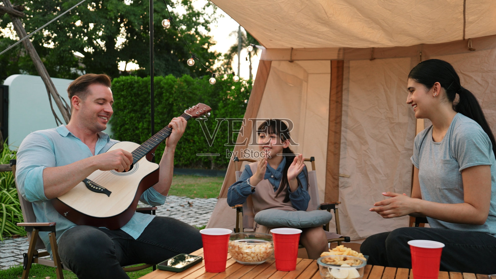 家庭露营。母女俩听着爸爸弹吉他。散度。照片摄影图片