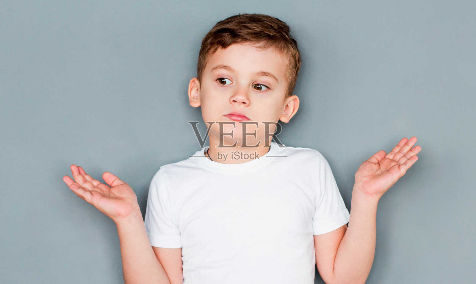 可爱的小男孩穿着休闲的白色t恤，手臂和双手举起，表情茫然而困惑。怀疑的概念。照片摄影图片
