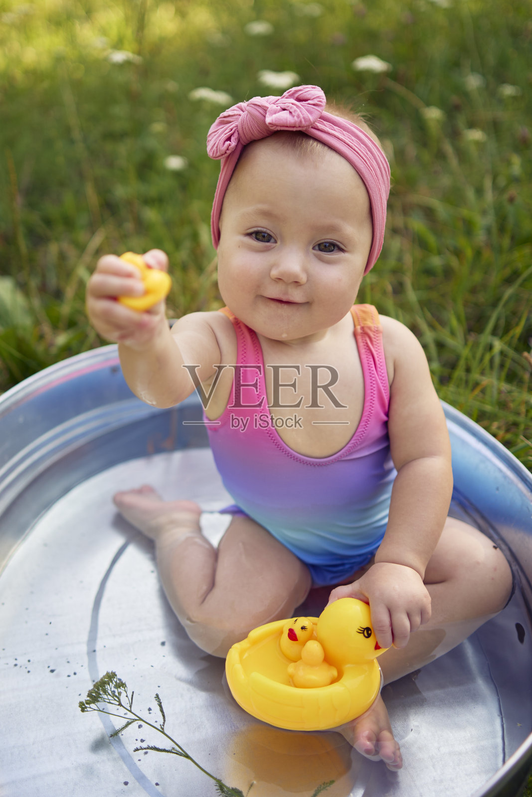 夏日花园里，一个婴儿在金属桶里和橡皮小鸭玩耍照片摄影图片