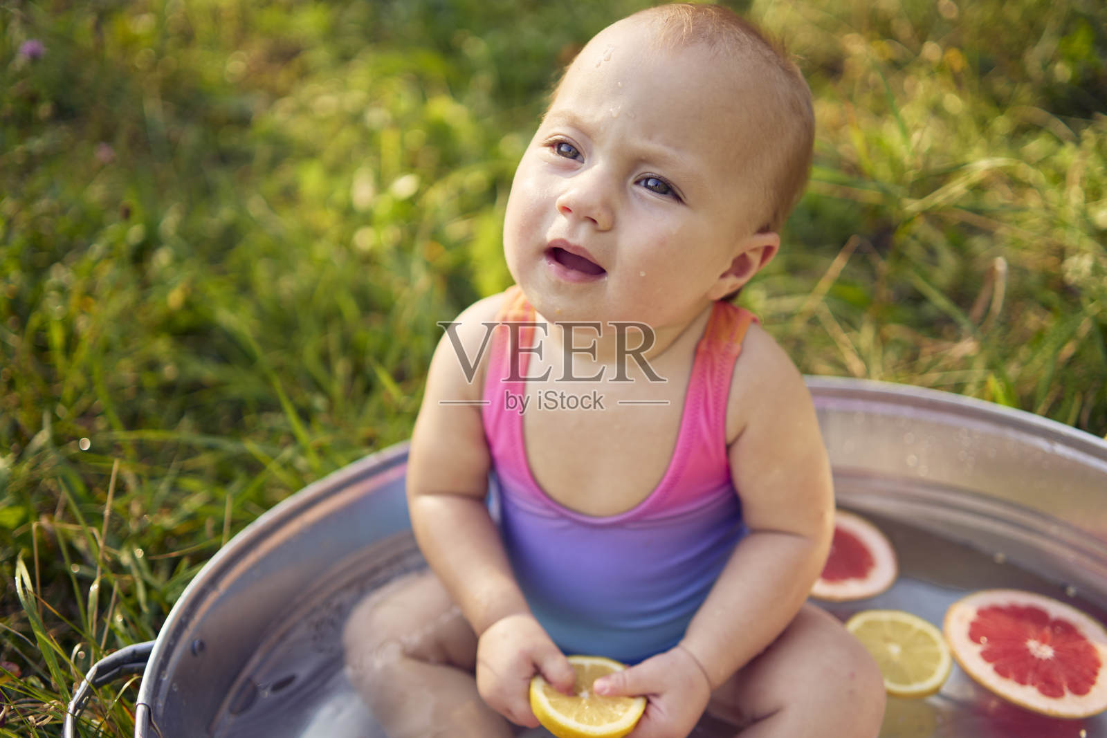 夏日花园里，一个婴儿在金属浴缸里玩柚子和柠檬片照片摄影图片
