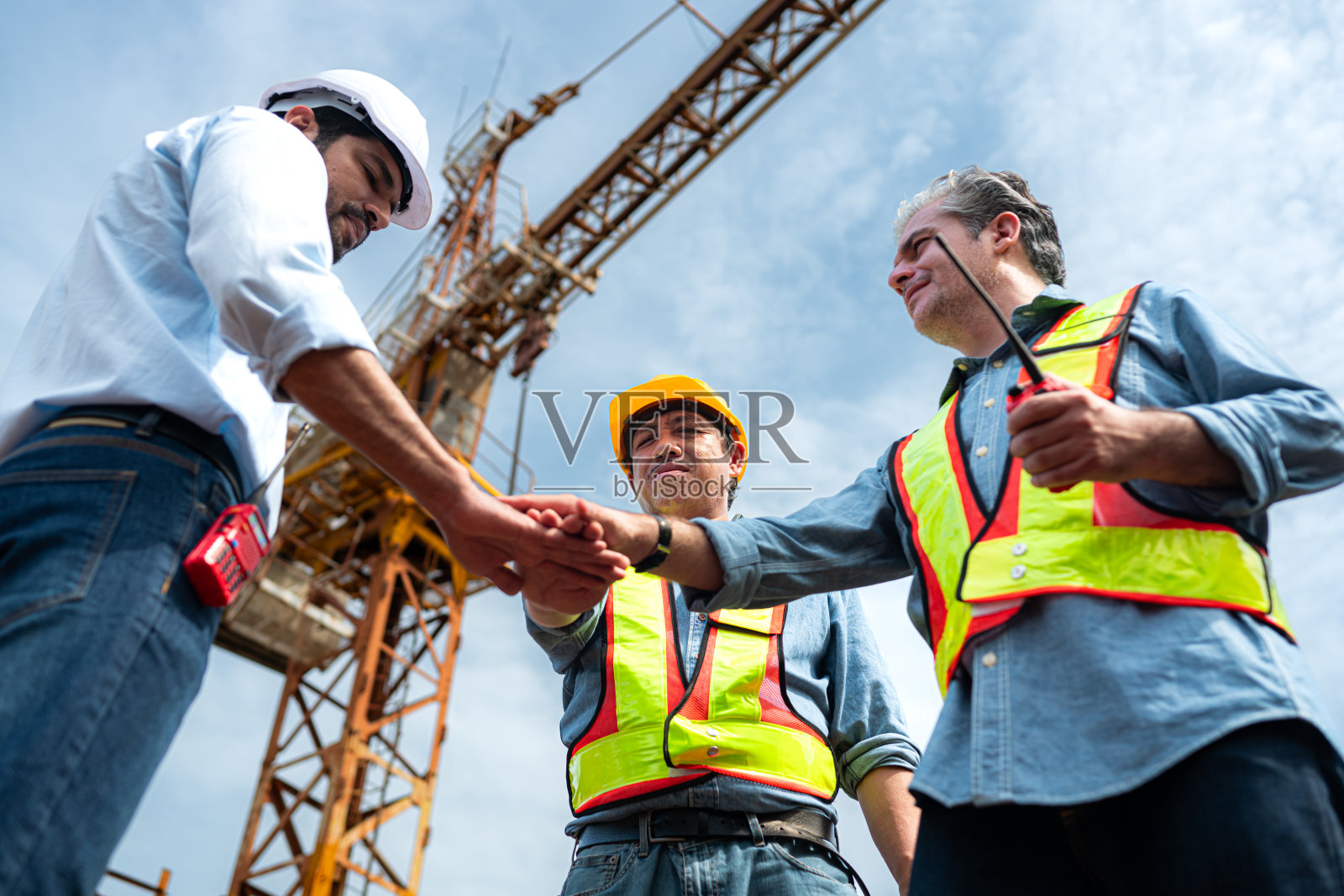 图为，工地上的工人们正在讨论施工进度，背景是塔吊照片摄影图片