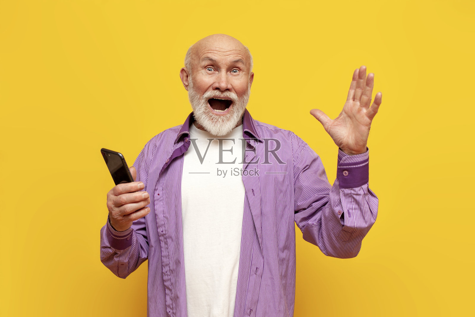惊讶的秃顶老爷爷使用智能手机，在黄色孤立的背景下高兴地尖叫照片摄影图片