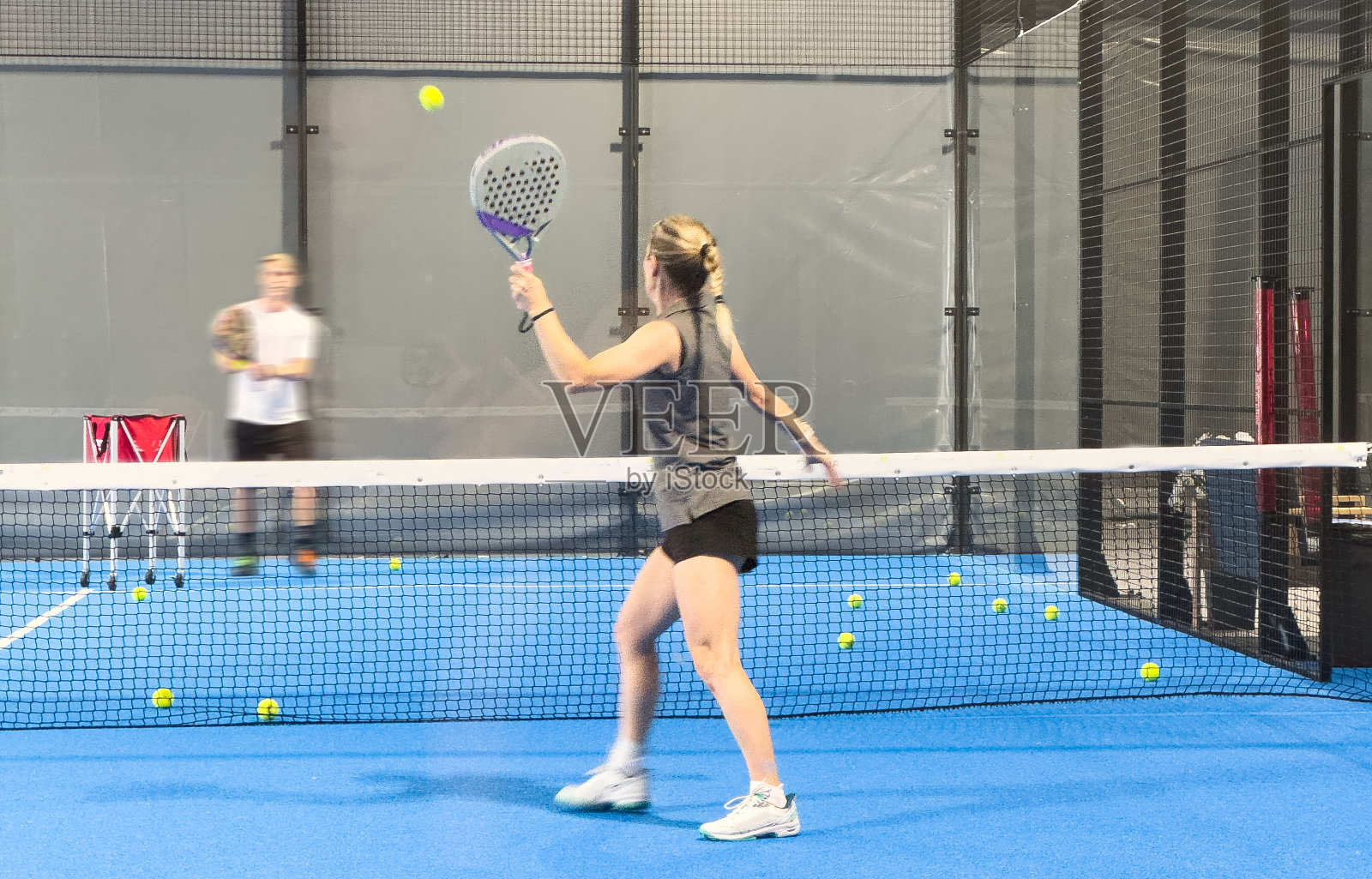 班长给一个女人上打板课，他的学生教练教小女孩如何在室内网球场打打板照片摄影图片