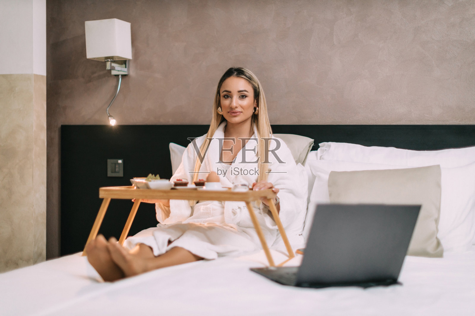 一个女人在床上用笔记本电脑，在酒店房间里吃早餐照片摄影图片