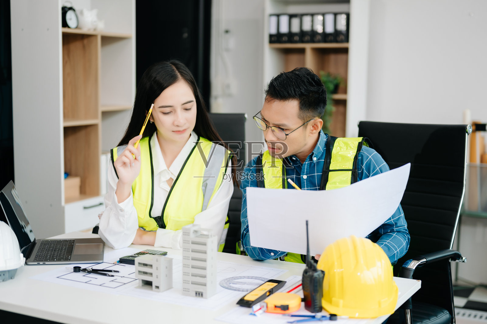 有创意的建筑师在办公桌旁的建筑工地投影着建筑项目的大图纸照片摄影图片