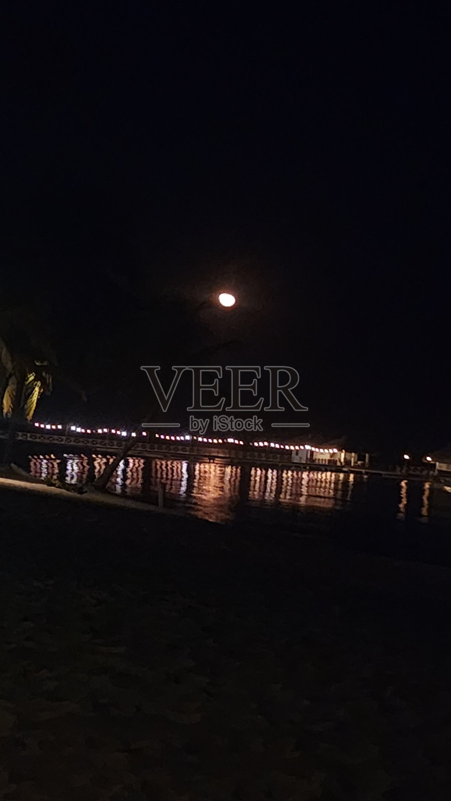 码头和灯光在夜晚的海上反射，月亮在上面。9:16背景照片摄影图片