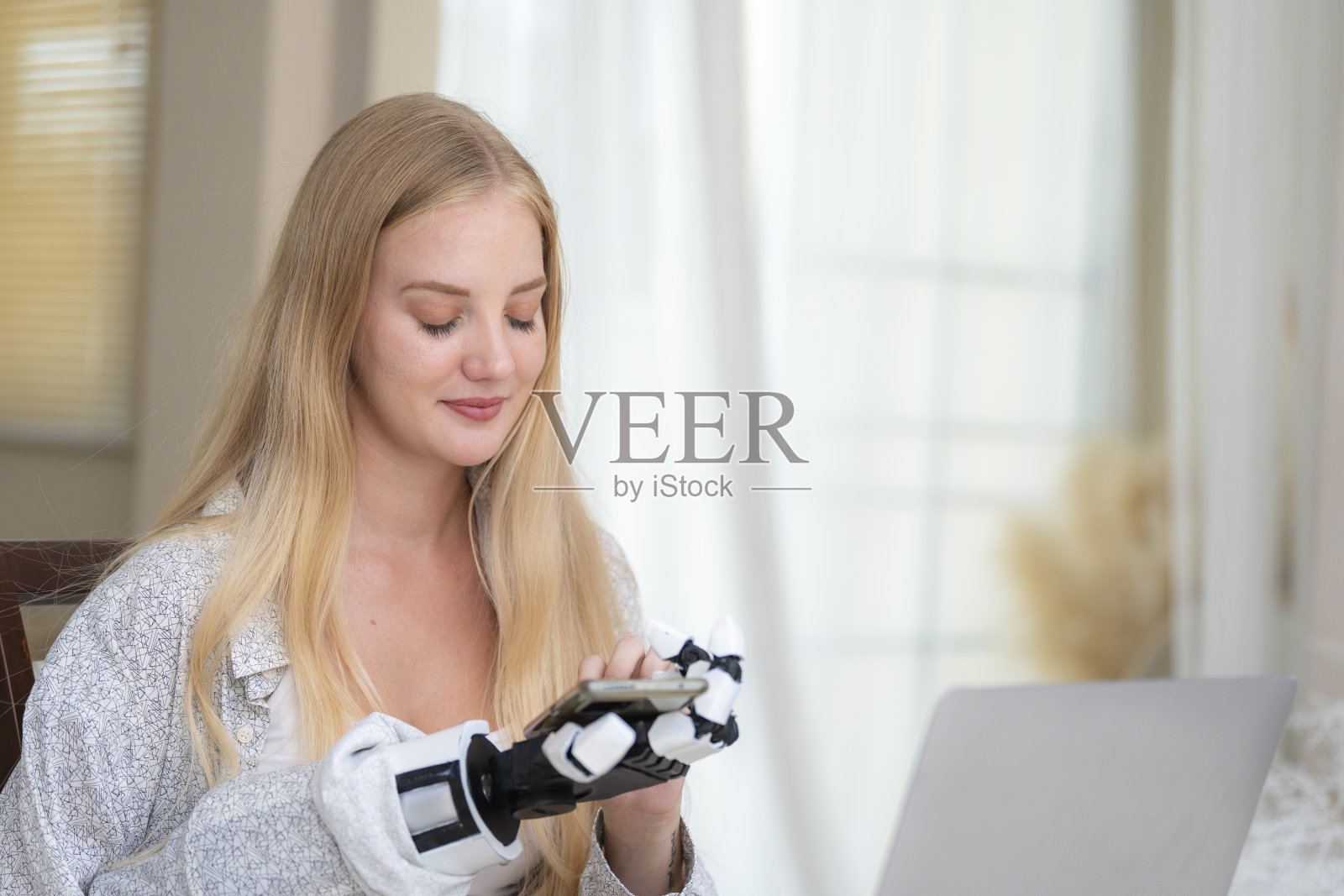 一名年轻女子正在使用附着在她身体上的机械假肢手在桌子上工作。她正在做电脑文件和通讯工作。一位女士试图控制家中的智能手臂。照片摄影图片