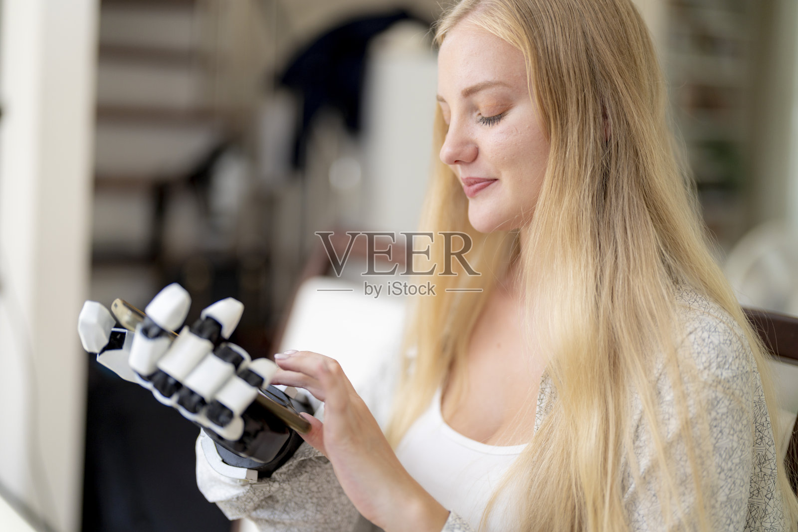 一名年轻女子正在使用附着在她身体上的机械假肢手在桌子上工作。她正在做电脑文件和通讯工作。一位女士试图控制家中的智能手臂。照片摄影图片