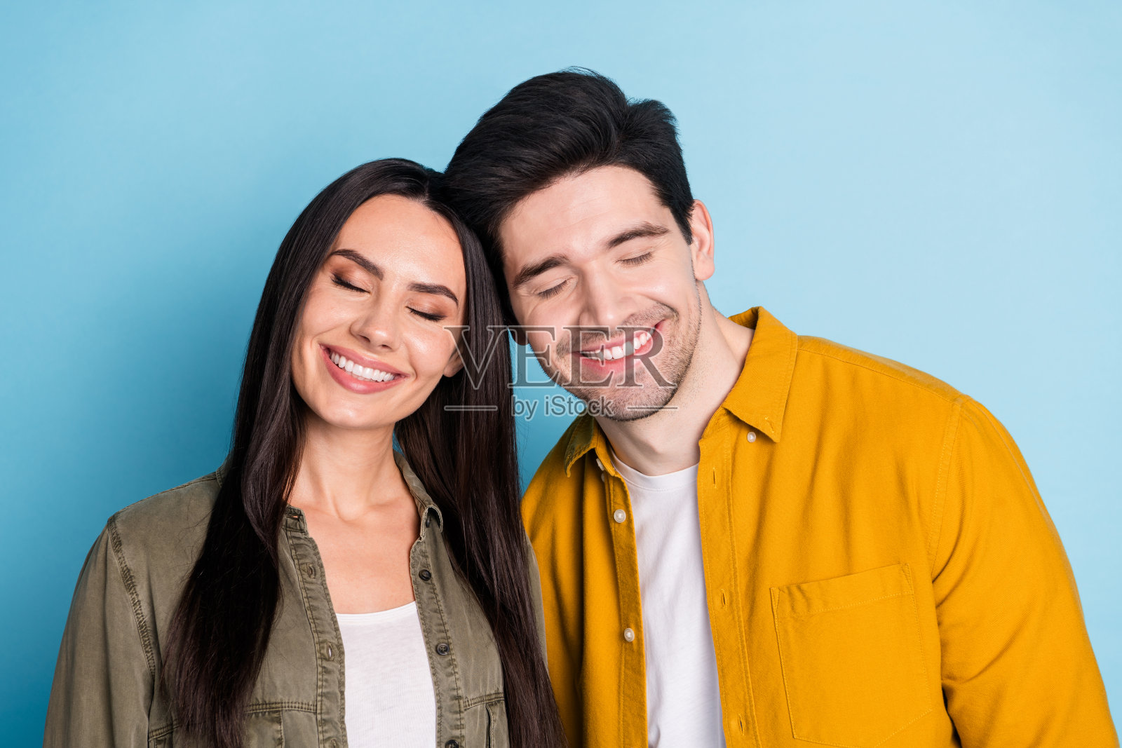 照片上的两个漂亮的年轻伙伴闭着眼睛碰着头，穿着衬衫孤立的蓝色背景照片摄影图片